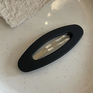 Close-up of minimalist black matte oval hair clip with silver metal snap mechanism