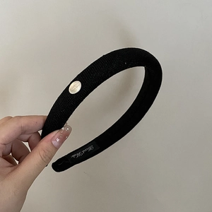 Détail d'un serre-tête rembourré noir avec plaque logo argentée et étiquette fait main