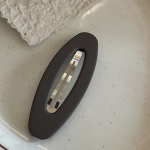 Detail of matte oval hair clip with silver metal spring on a ceramic plate