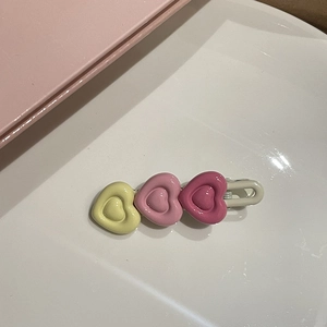Dettaglio di un fermaglio per capelli con tre cuori 3D sfumati rosa e finitura lucida