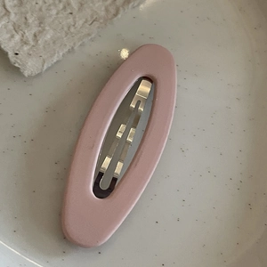 Detail view of pink matte oval hair clip placed on a decorative ceramic plate