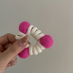 Primo piano di un elastico a spirale bianco con tre sfere di lana magenta tenuto in mano