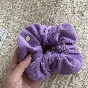 Close-up of purple towel fabric scrunchie with engraved golden handmade metal tag