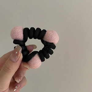 Elastico per capelli a spirale con tre palline di lana rosa tenuto in mano