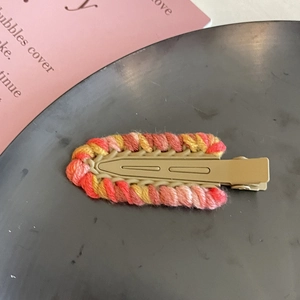 Dettaglio di un fermaglio per capelli in lana colorata intrecciata a mano su base kaki