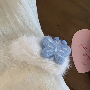 Dettaglio di un fermaglio per capelli in peluche bianco con farfalla in feltro azzurro