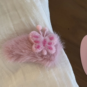 Dettaglio ravvicinato di una molletta per capelli a farfalla in peluche rosa con ricamo