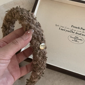 Detailed macro view of the thick brown tweed headband with a gold vintage emblem accent