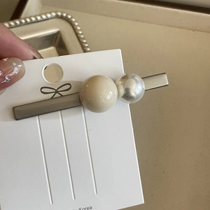 Pince à cheveux de style coréen avec perles crème et blanches tenue à la main