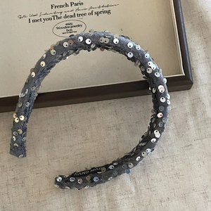 Handmade grey velvet headband with silver sequins and hand-made tag on linen background