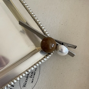Détail d'une pince à cheveux argentée avec des perles marron foncé et blanches