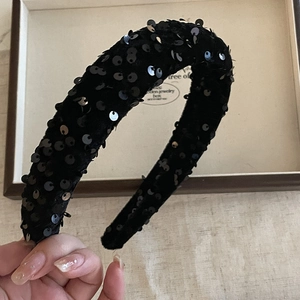 Detailed close-up of a thick black headband with shimmering sequins held by hand