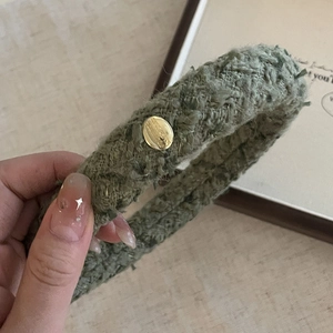 Close-up of a dark green tweed headband featuring a polished gold oval metal buckle