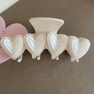Close-up of beige heart-shaped claw clip with glossy finish on a textured background