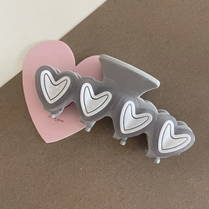 Detail view of large gray hair claw clip with white-outlined 3D heart patterns
