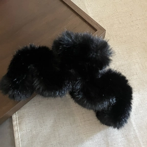 Detail of fluffy black plush hair scrunchie with soft faux fur texture on a woven mat