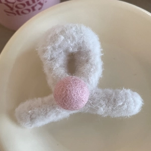 Détail d'une pince à cheveux en peluche blanche douce avec une décoration boule rose