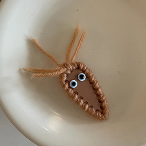 Detail of a handmade brown knitted hair clip with cute cartoon eyes on a ceramic plate