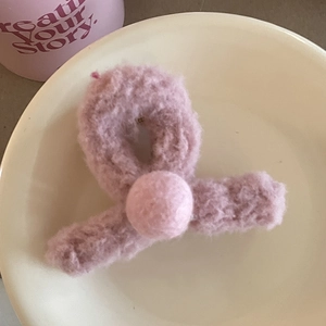 Détail d'une pince à cheveux en peluche rose avec une décoration de boule douce