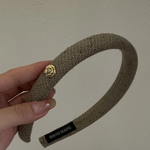 Detail of khaki knitted headband with golden camellia metal flower and handmade label
