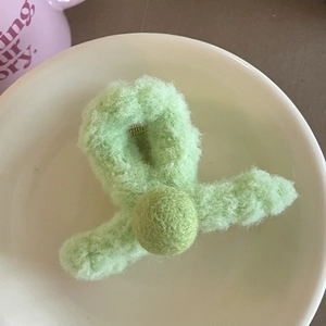 Vue de dessus d'une pince à cheveux en peluche vert clair avec pompon dans un bol blanc