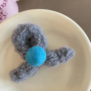 Détail d'une pince à cheveux en peluche grise avec une boule de feutre bleu contrasté