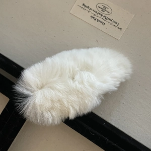 Détail d'une pince à cheveux en peluche blanche douce sur un fond esthétique épuré