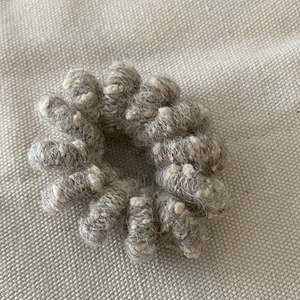 Detailed close-up of a warm wool-wrapped spiral hair tie in grey and beige knit texture