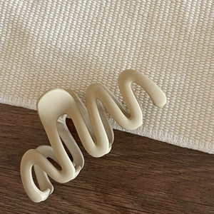 Minimalist beige matte large wavy hair claw clip with modern S-shaped design on a woven mat