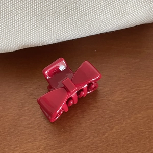 Detail view of a small wine red bow-shaped claw clip on a rustic wooden table background