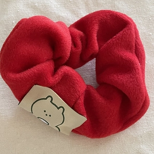 Détail d'un chouchou épais en peluche rouge avec étiquette ours sur tissu texturé