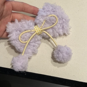 Dettaglio fermaglio per capelli con fiocco di peluche viola, nastro giallo e pompon