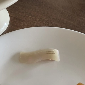 Detail of a wavy cream hair clip with a pearlescent finish and France Handmade gold lettering
