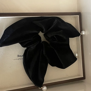 Chouchou élégant en velours noir avec trois perles pendantes sur plateau en bois
