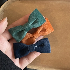 Close-up of velvet bow hair clips in dark green, burnt orange, and navy blue
