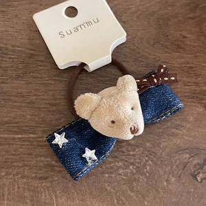 Detail showing plush bear motif and denim bow hair tie with silver star studs on wood