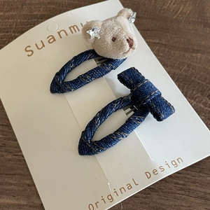 Detail of plush bear and denim bow hair clip set with contrast stitching on white card