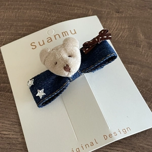 Detail of denim bow hair clip with plush bear head and silver star accents on wood surface