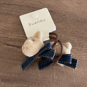 Detail view of plush bear hair tie with denim bow and elastic band on wooden table
