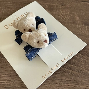 Detailed view of plush bear and denim bow hair clip with gold stitching on white card