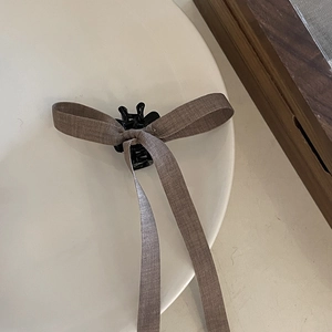 Close-up of a brown ribbon bow hair claw clip with long streamers on a white plate