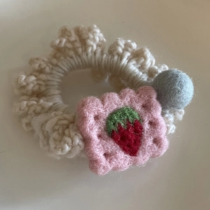 Detail of handmade crochet hair tie featuring strawberry embroidery and felt ball ornament