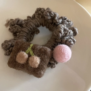 Close-up of handmade crochet hair scrunchie with felt cherry and pink ball details