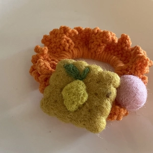 Detailed close-up of handmade orange knit hair tie with plush ball and fruit pattern texture