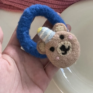 Detailed view of a handmade wool felt hair tie featuring a cute brown bear with a blue hat