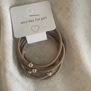 Set of 5 elastic hair ties with gold beads on display card against linen background