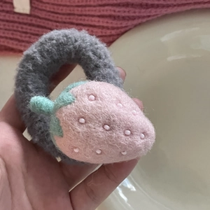 Close-up of grey plush hair scrunchie featuring a pink knit strawberry with green leaves