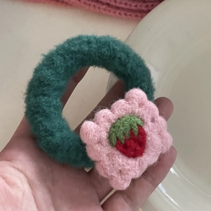 Detail of dark green crochet hair tie with pink flower and strawberry pattern