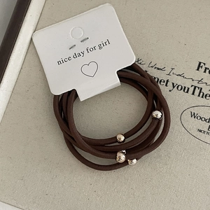 Close-up of brown high-elastic hair ties set with metallic beads on white display card