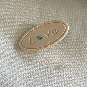 Barrette ovale crème avec gravure Love et strass bleu sur un fond en toile beige